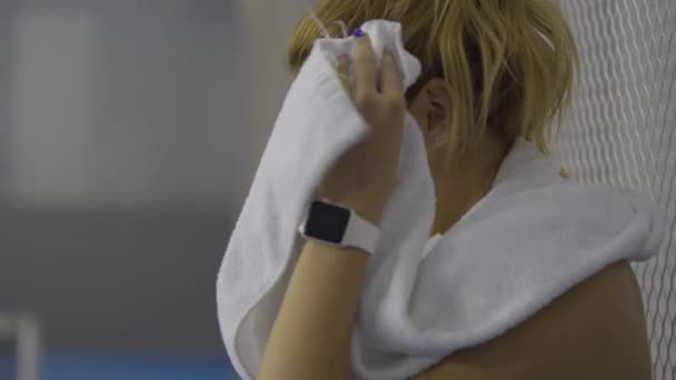 Detailní pohled na mladou zpocenou sportovkyni, která si utírá obličej bílým ručníkem. Vyčerpaná mladá běloška po tréninku nebo cvičení v tělocvičně. Koncept únavy a sportu. — Stock video