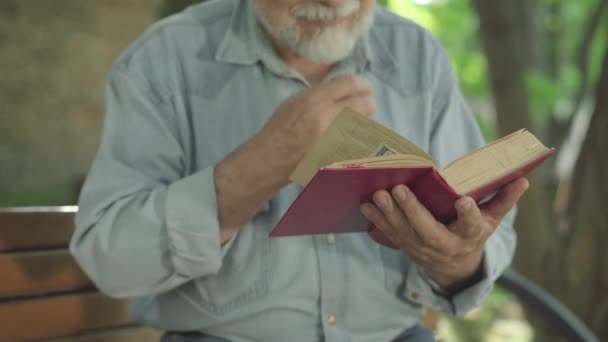 Ireconhecível absorvido velho homem lendo livro ao ar livre e sorrindo. Feliz despreocupado relaxado Caucasiano aposentado desfrutando hobby no ensolarado parque de verão. Sênior inteligente interessado em literatura. — Vídeo de Stock