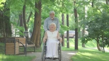 Neşeli engelli kadın ve Sunny Park 'ta tekerlekli sandalyeli yaşlı adamın geniş açılı görüntüsü. Neşeli Kafkas bir çift emeklinin portresi eğleniyor. Mutlu eş ve koca gülüyor ve gidiyor..