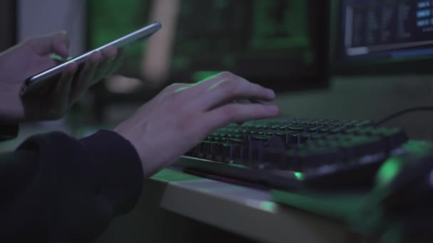 Oigenkännlig ung programmerare med smartphone skriva på datorns tangentbord. Självsäker manliga kaukasiska hacker kodning eller hacka webbplats. Koncept för Internetsäkerhet och it-angrepp. — Stockvideo