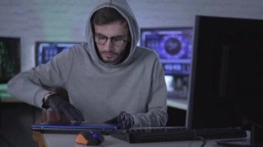 Kendine güvenen ciddi bir adam ofise birden fazla bilgisayarla giriyor, dizüstü bilgisayarı açıyor ve klavyede daktilo kullanıyor. Siyah eldivenli beyaz erkek hacker portresi bilgisayar virüsü yayıyor ya da bilgi sızdırıyor..