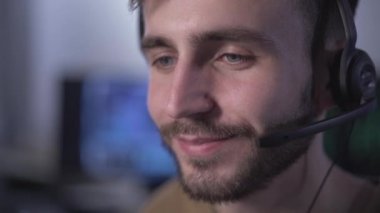 Kulaklık danışmanlığı yapan yakışıklı genç bilişim uzmanının yakın plan yüzü. Kulaklıkla konuşan ve gülümseyen beyaz bir adamın portresi. Profesyonel destek servisi.