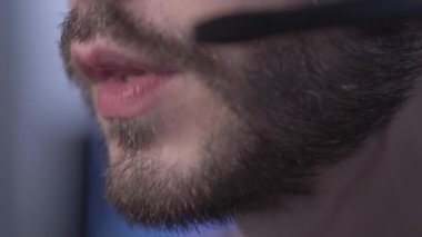 Kulaklık takmış ciddi sakallı beyaz adamın dudakları konuşuyor. İletişim merkezinde çalışan tanınmayan genç profesyonel veya teknik destek.