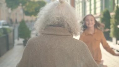 Uzun gri saçlı yaşlı bir adamın, gün ışığında şehir sokağında oturmuş, koşuşturan ve büyükbabaya sarılan iki neşeli çocuğun arka görüntüsü. Kafkasyalı büyükanne ve büyükbabası dışarıda torunlarıyla buluşuyor..