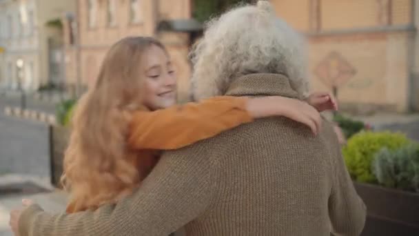 Счастливые дети обнимают белого мужчину-пенсионера и улыбаются в камеру. Портрет радостных внуков, встречающихся с дедушкой с длинными седыми волосами в солнечный день на открытом воздухе. Детство и пенсия. — стоковое видео