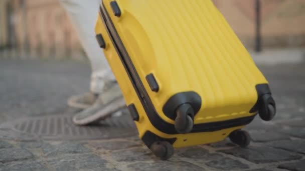 Caméra suit sac de voyage jaune roulant sur le trottoir sur la rue de la ville. Touriste masculin méconnaissable se promenant avec des bagages dans l'ancienne ville européenne. Concept de voyage et de tourisme. — Video