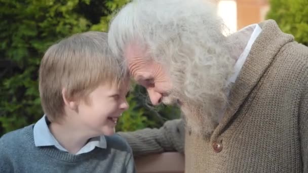 Vue latérale rapprochée de joyeux grand-père et petit-fils frottant les nez à l'extérieur. Portrait d'homme aux cheveux gris âgé caucasien joyeux et riant petit garçon mignon s'amusant. — Video