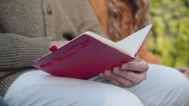 Närbild av ledande manliga kaukasiska händer hålla bok. Oigenkännlig pensionär läsning på solig dag utomhus. Pensionering och hobbykoncept. — Stockvideo