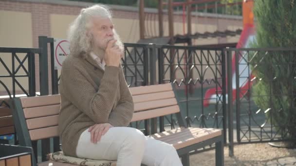 Schattige blanke jongen met bal rennend naar senior man zittend op bank op zonnige dag buiten. Portret van vrolijke grijsharige grootvader genietend van zomerweekend met kleinzoon buitenshuis. — Stockvideo