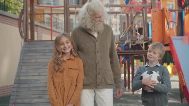 Familia multigeneracional feliz posando en el patio al aire libre. Retrato de hombre mayor caucásico alegre, niño y niña mirando a la cámara y sonriendo. Unidad y ocio familiar. — Vídeo de stock