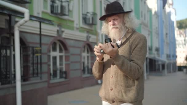 ヨーロッパの都市で写真を撮るためにカメラを調整する深刻なシニア男性観光客。旅行中に帽子の撮影現場で自信を持ってリラックスした白人男性の肖像画。引退・レジャー. — ストック動画