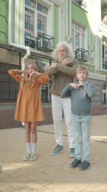 Dikey video, şehrin sokaklarında neşeli çoklu aile dansları. Güneşin altında dans eden Kafkas büyükbaba ve torunlarının tasasız portresi..