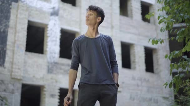 Addicted mixed-race man drinking beer on slum or urban ruins. Portrait of young alcoholic at abandoned ruined urban building. Alcohol abuse and vagrancy. — Stock Video