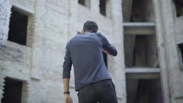 Back view of aggressive young man drinking beer and shouting at abandoned slum. Mixed-race alcoholic yelling on ruins drinking alcohol from bottle. Aggression and abuse concept. — Stock Video