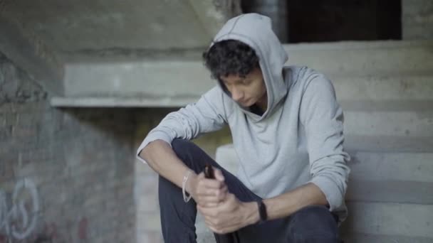 Portret młodego, nastoletniego alkoholika siedzącego na schodach na ruinach i pijącego piwo. Przygnębiony mieszany uchodźca mieszkający w getcie. Koncepcja bezdomności i dorastania. — Wideo stockowe