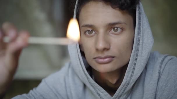 Close-up face of mixed-race boy with brown eyes blowing out match and looking at camera. Portrait of thoughtful depressed teenager planning setting fire. Adolescence and crime concept. — Stock Video