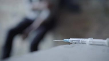 Arka planda bulanık keş kıvranan şırınganın yakın çekimi. Varoşlardaki şehir harabelerinde tanımlanamayan aşırı dozda uyuşturucu bağımlısı. Uyuşturucu ve madde bağımlılığı.