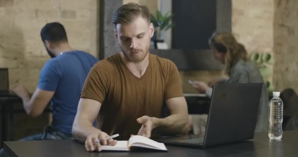 Kafkasyalı bir gencin portresi arka planda bulanık adamlarla çevrimiçi çalışıyor ya da ders çalışıyor. Bilgisayarda internette sörf yapan iş adamı ya da öğrenci. E-öğrenme. Sinema 4k ProRes Merkezi. — Stok video