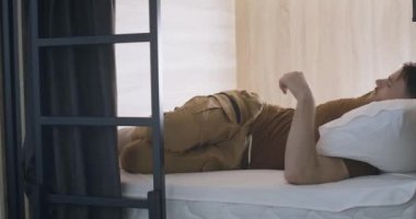 Akıllı telefondan alarm kurup uyuyan yorgun genç adam. Pansiyonda yatakta yatan yakışıklı beyaz bir adam. Yaşam tarzı. Sinema 4k ProRes Merkezi.