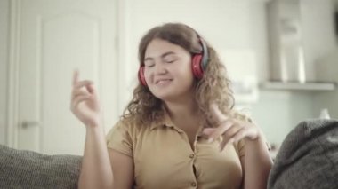 Evde koltukta oturmuş kulaklıkla müzik eşliğinde dans eden tombul bir kadının portresi. Hafta sonları evde hobi edinen kaygısız beyaz kadın. Boş zaman konsepti.