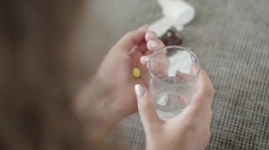 Sarı hap ve bir bardak su tutan genç kadınların üst açı görüntüsü. Viral enfeksiyon ya da kronik hastalıklara karşı ilaç alan büyük beden hasta bir kadın. İlaç ve sağlık hizmetleri.