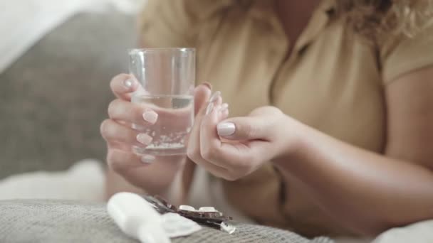 Närbild av kvinnliga händer håller piller och glas vatten. Oigenkännlig sjuk kaukasisk kvinna med droger inomhus. Ung knubbig dam med mediciner hemma. Medicin och hälsovård. — Stockvideo