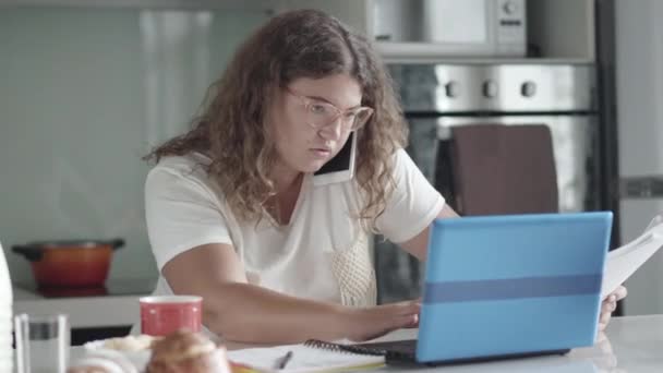 Femme d'affaires obèse occupée parlant au téléphone et tapant sur le clavier de l'ordinateur portable à la maison. Portrait de femme caucasienne concentrée travaillant en ligne pendant le confinement. Freelance et télétravail. — Video