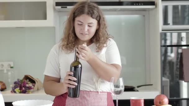 Morena gordo mulher branca abertura garrafa e derramando vinho tinto em vidro. Retrato de tiro do meio de sorrir senhora plus-size degustação de bebida cara em casa nos fins de semana. Conceito de álcool. — Vídeo de Stock