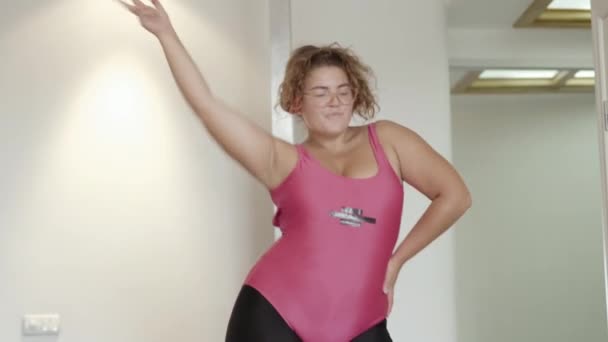 Retrato de mujer regordeta alegre bailando con música en auriculares. Joven y alegre dama caucásica en ropa deportiva divirtiéndose en casa. Concepto de deporte y hobby. — Vídeos de Stock