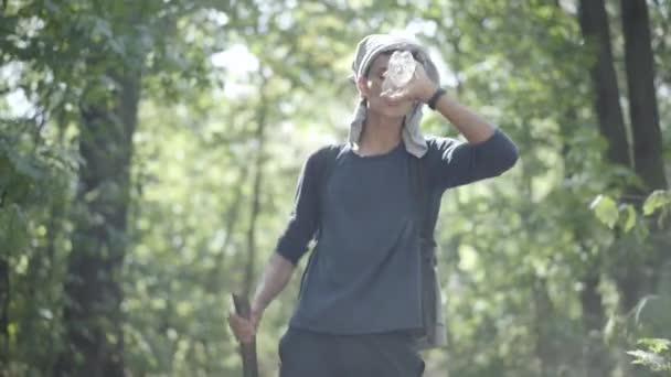 Giovane rifugiato cauto che cammina alla luce del sole nella verde foresta estiva e beve acqua rinfrescante. Lunga strada di emigrati lungo i boschi. Emigrazione e concetto di fuga. — Video Stock