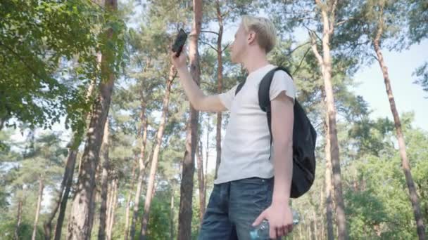 Portrét mladého pohledného bělocha, který se snaží najít mobilní síť v lese. Starostlivý muž turista turistika pomocí smartphone venku na slunci během cesty. — Stock video