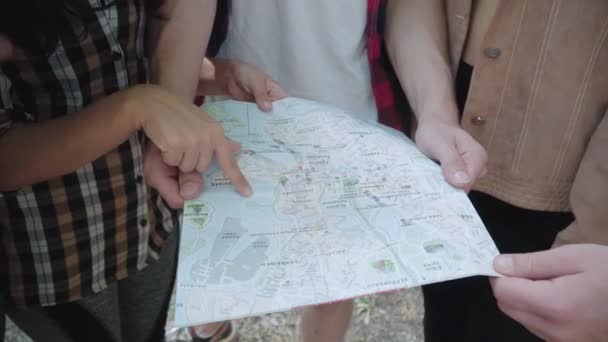 Close-up of paper map in male hands with unrecognizable men and women pointing and gesturing. Group of young Caucasian tourists hiking on sunny summer day outdoors. Eco-tourism concept. — Stock Video