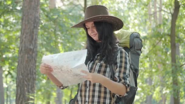 Porträtt av vacker positiv kaukasisk kvinna med turist ryggsäck undersöker papperskarta och lämnar. Leende charmig kvinnlig resenär njuter av vandring på solig sommardag utomhus. — Stockvideo