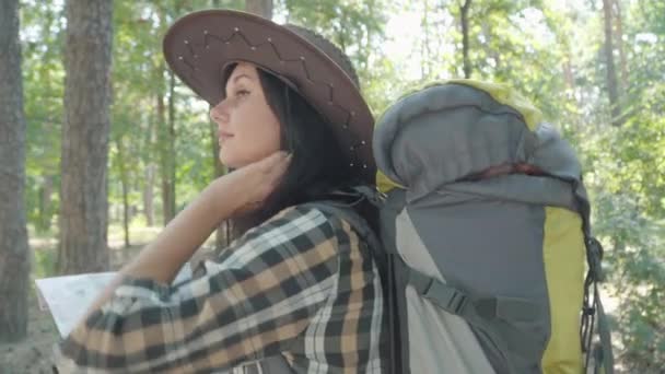 Charmante junge kaukasische Touristin mit Landkarte, die sich im sonnigen Wald umsieht und weggeht. Porträt einer selbstbewussten Frau, die im Sommer im Freien wandert. Reisende genießen Schönheit der Natur. — Stockvideo