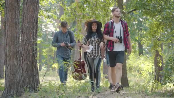 Group of cheerful young friends hiking on sunny summer day outdoors as beautiful Caucasian woman sprain foot. Young men and women taking care of friend. Hiking of carefree people in forest. — Stock Video