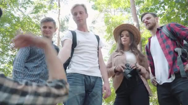 Вид снизу на уверенного молодого человека, протягивающего руку павшему другу в солнечном лесу. Группа веселых кавказцев поддерживает женщину с травмой лодыжки. Туризм и туризм. — стоковое видео