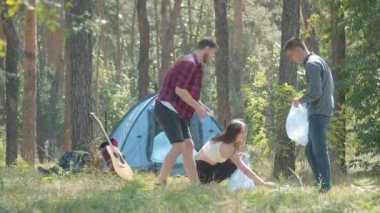 Kamp yaptıktan ve beşlik çaktıktan sonra yaz ormanı çayırlarını temizleyen genç dostların geniş açılı portresi. Çöp torbasında çöp toplayan beyaz kadın ve erkekler. Ekoloji kavramı.