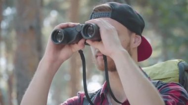 Dürbünle dışarıyı seyreden kendine güvenen yakışıklı adamın yakın çekimi. Güneşli yaz ormanlarında yürüyüş yapan gri gözlü, sakallı beyaz adamın portresi. Yaşam tarzı ve turizm konsepti.