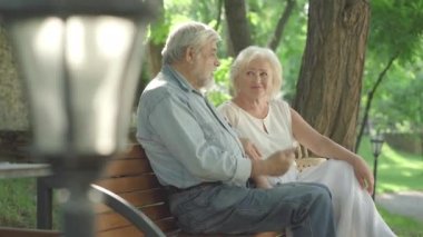 Güneşli parkta gevşemiş emeklilerin sohbetlerine ve kahkahalarına yan bakış. Kıdemli Kafkasyalı karı koca bankta oturup konuşuyorlar. Mutlu yaşlı çift dışarıda yaz gününün tadını çıkarıyor..