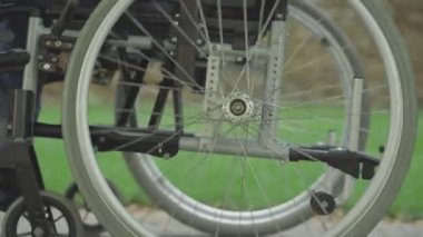 Tekerlekli sandalyenin yan görüntüsü dışarıda dönüyor. Güneşli yaz parkında engelli ya da felçli birine binen tanınmamış bir kadın. Hasta insanların aktif yaşam tarzı.