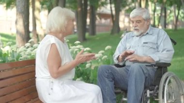 Sunny Park 'ta yaşlı bir kadınla konuşan tekerlekli sandalyedeki pozitif felçli bir adamın portresi. Bir çift kaygısız emeklinin yaz günü dışarıda sohbet etmesi. Mutluluk ve yaşam tarzı.