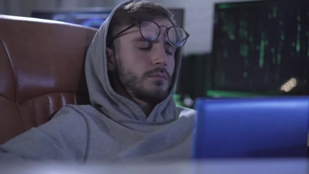 Крупный план портрета кавказского юноши, просыпающегося, надевающего очки и начинающего печатать на клавиатуре ноутбука. Серьезное исчерпанное программирование онлайн или хакерское хакерство веб-сайта. — стоковое видео