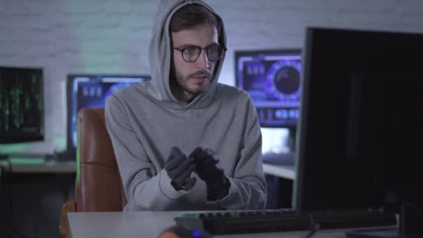 Цілеспрямований чоловік в окулярах одягає чорні рукавички і друкує на клавіатурі комп'ютера. Портрет чоловіка, який краде інформацію з офісу або зламує пароль безпеки. — стокове відео