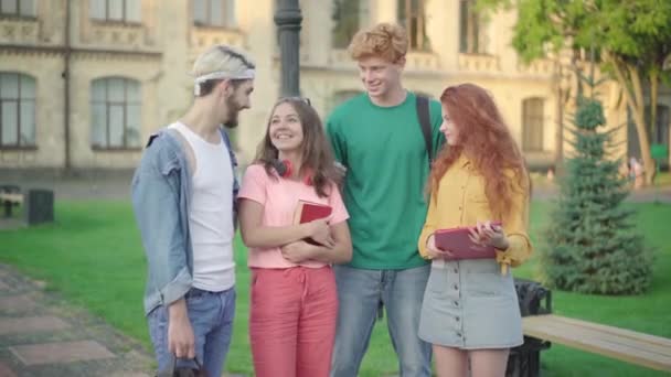 Caméra approche du groupe de jeunes étudiants universitaires heureux debout sur le campus. Hommes et femmes caucasiens regardant la caméra et souriant. Concept d'amitié et d'éducation. — Video