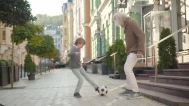 Mutlu büyükbaba ve torununun şehir sokaklarında futbol oynayıp, dışarıda torunuyla eğlenen Kafkas büyükbabalarının portresini çekerken geniş açılı bir çekim..