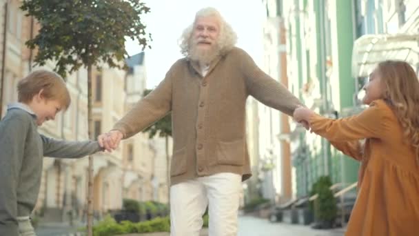 Retrato de um idoso sorridente a falar com crianças a puxar a mão e a apontar para longe. Feliz avô caucasiano se divertindo com netos ao ar livre no dia ensolarado de verão. — Vídeo de Stock
