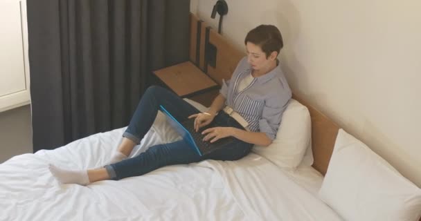 集中白人の美しい女性のトップビューは、ベッドの上に座って、紅茶やコーヒーとカップをもたらすアフリカ系アメリカ人の男を愛するとしてノートパソコンのキーボードを入力します。異人種間のカップルの幸せな関係 — ストック動画