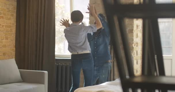 Alegre jovem casal interracial dançando no quarto e sorrindo. Homem afro-americano positivo e mulher caucasiana se divertindo nos fins de semana ensolarados em casa. Relacionamento feliz multiétnico. — Vídeo de Stock