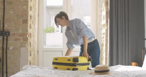 Mulher bonita confiante zíper saco de viagem amarelo e deixando quarto de hotel ou quarto com bagagem. Jovem encantador turista caucasiano feminino com bagagem dentro de casa. — Vídeo de Stock