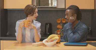 Kafkasyalı genç kadın ve Afro-Amerikalı erkek portakal bardaklarından çay ya da kahve içip sohbet ediyorlar. Mutlu, rahat, ırklar arası bir çift sabah evde mutfakta sohbet ediyor..